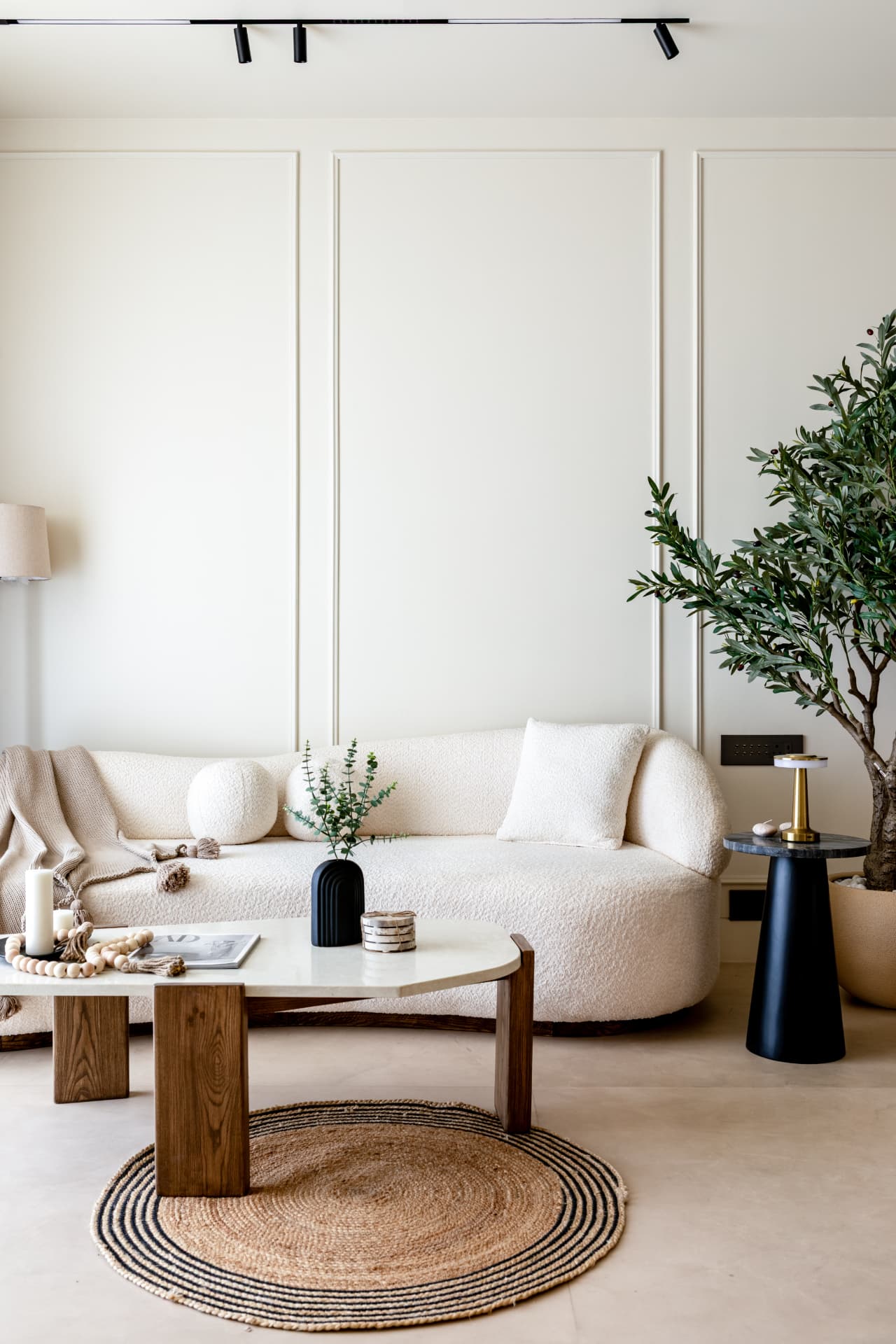 Curved bouclé sofa against panelled ivory wall with olive tree and jute rug