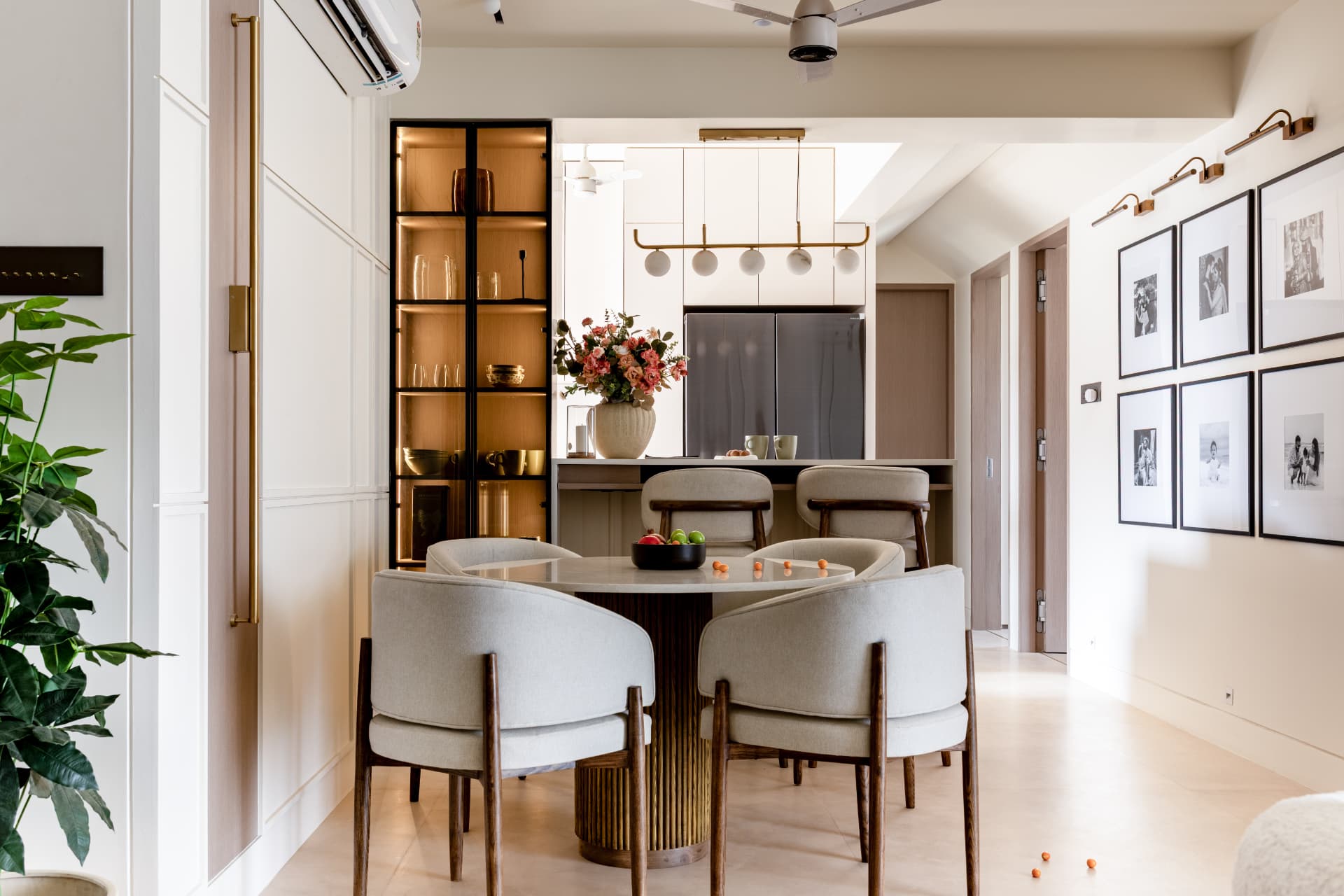 Round fluted dining table with backlit glass cabinet and gallery wall